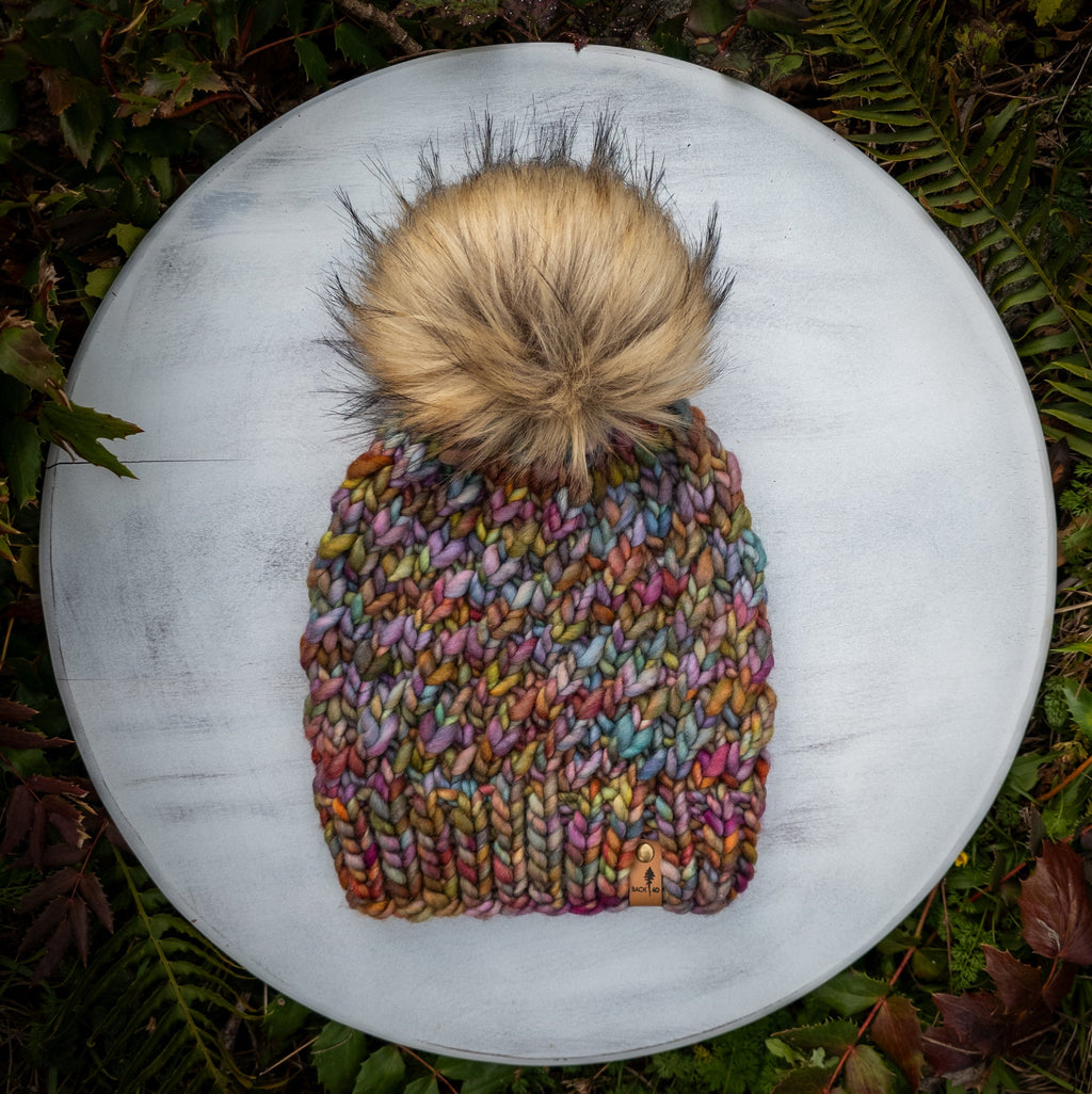 Multicolored knitted beanie with a golden faux fur pom pom.