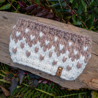 Knitted pouch with a pattern on a wooden log surrounded by greenery