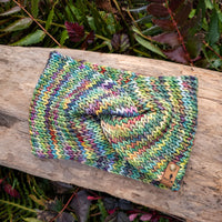 Multicolored knitted pouch on a wooden log with green foliage in the background