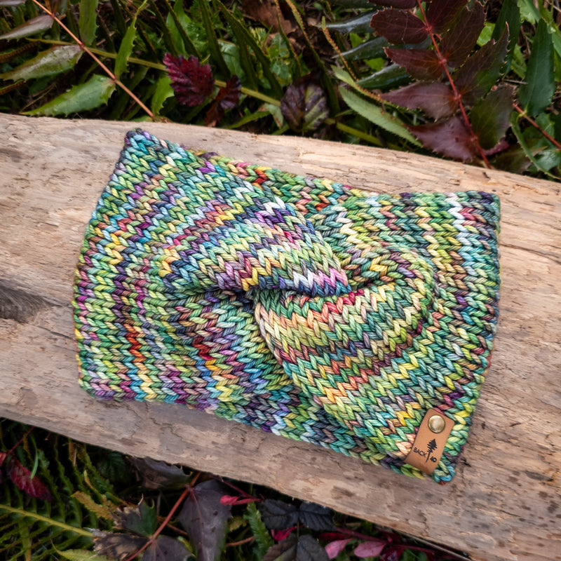Multicolored knitted pouch on a wooden log with green foliage in the background