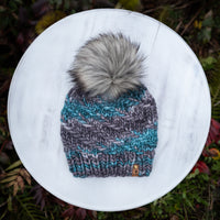 Knitted beanie with a fur pom-pom on a white surface with a natural background